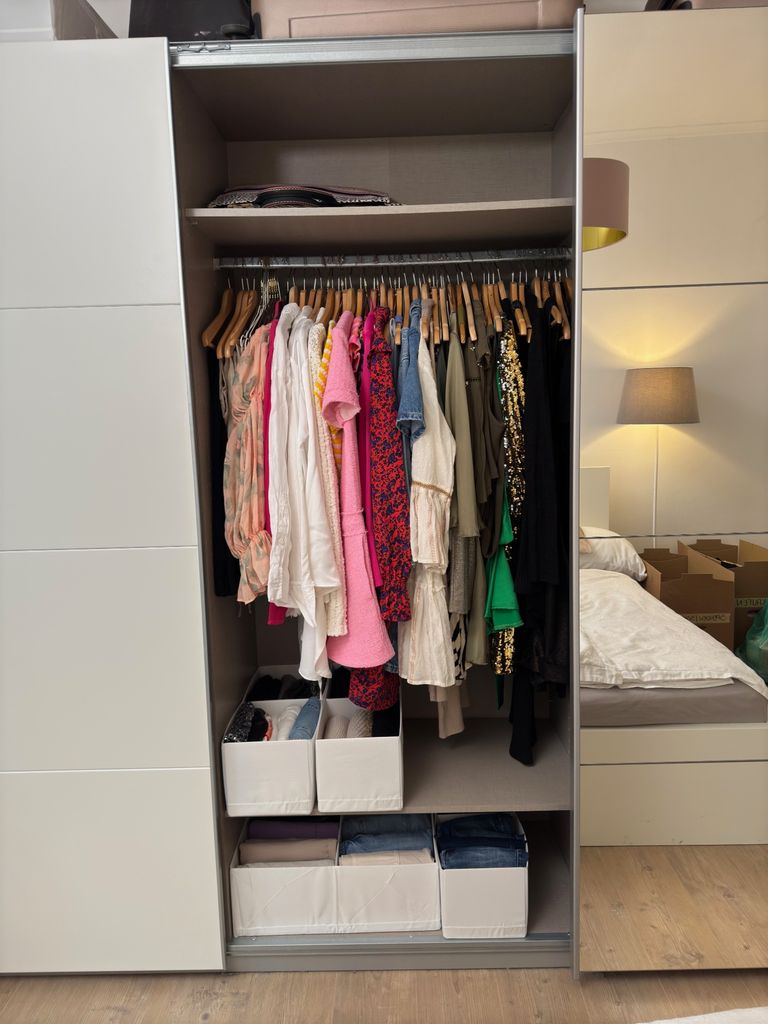 Aufgeräumter Kleiderschrank mit sortierter Kleidung auf Holzbügeln und weißen Stoffboxen