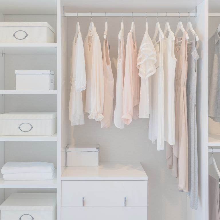 Ordentlicher weißer Kleiderschrank mit Kleidung in Pastelltönen auf Bügeln und Aufbewahrungsboxen