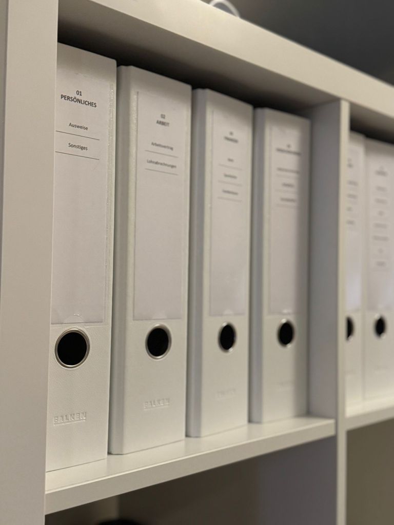Weiße Aktenordner mit einheitlichen Rücken-Beschriftungen in einem Regal