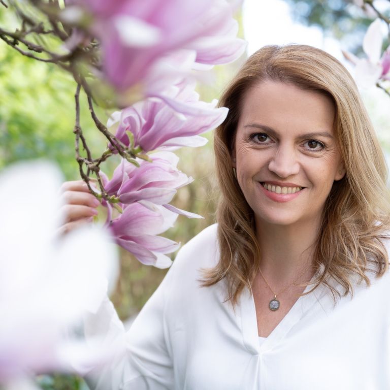 Adina Ortjohann lächelt zwischen rosafarbenen Magnolienblüten, sie trägt eine weiße Bluse